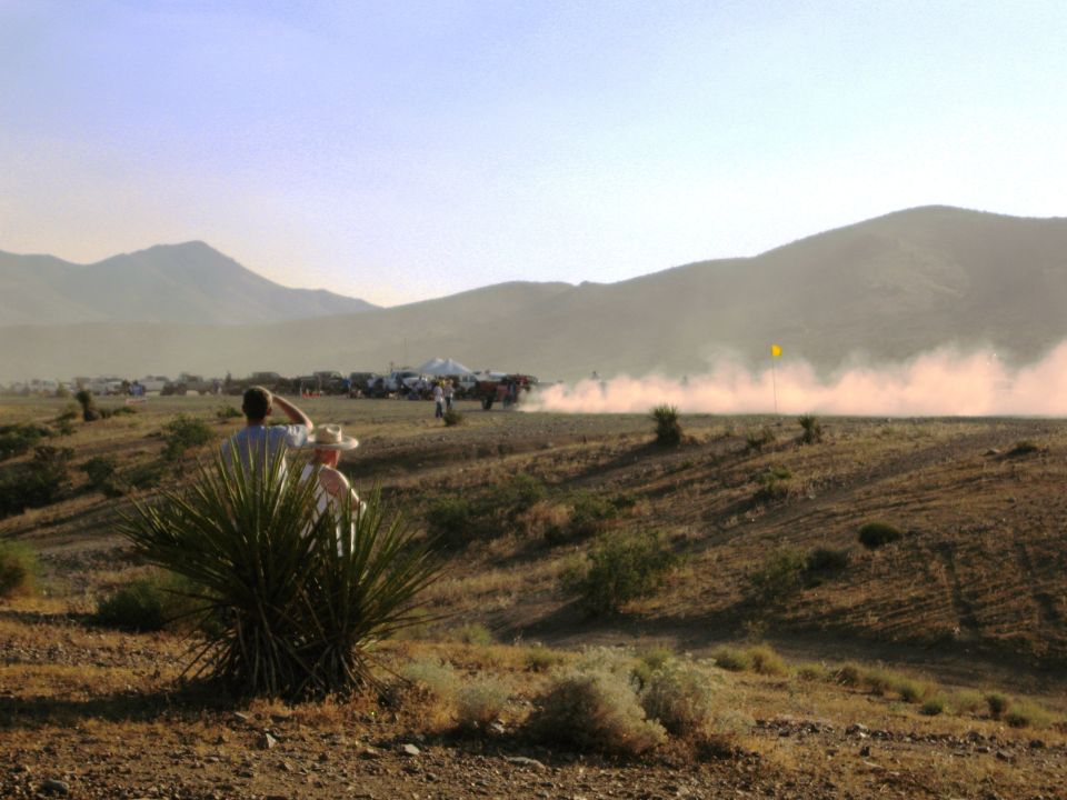 Spectators watch a dusty desert race with multiple vehicles in the distance