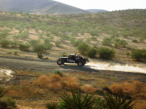 1986 Ford Bronco - A modified off-road truck races down a dusty desert track, leaving a trail of dust in its wake.