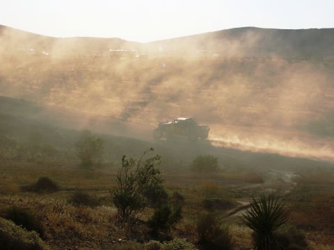 1986 Ford Bronco - A vehicle speeds across a dry, dusty landscape under a hazy sky.