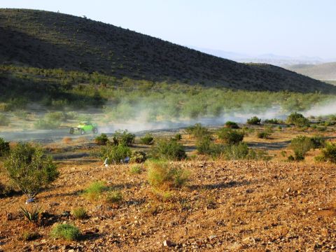 1986 Ford Bronco - A bright green off-road buggy navigates a dusty desert track, leaving a trail of dust in its wake under a clear sky.