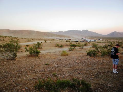 1986 Ford Bronco - A wide desert landscape with a gathering of vehicles in the distance and a man standing on the right.