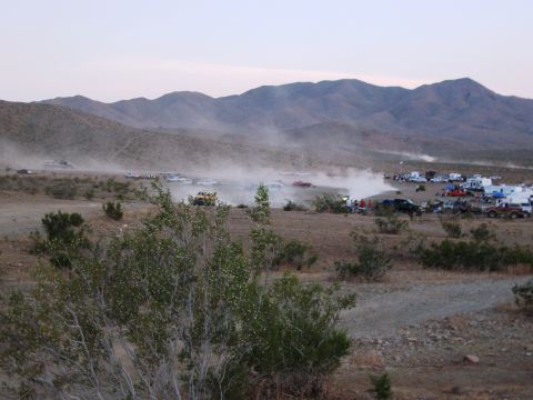 1986 Ford Bronco - Multiple vehicles participate in a desert race, kicking up significant dust as spectators watch.