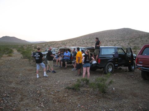 1986 Ford Bronco - Several people stand and sit around multiple vehicles in a dry, arid landscape during the day.