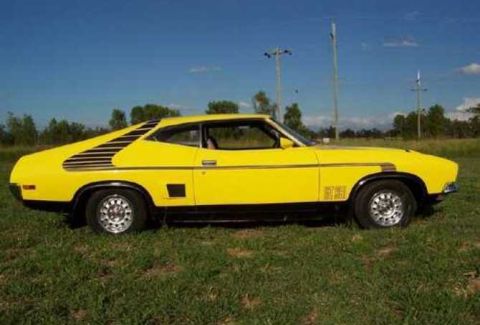 1991 Ford Bronco - A yellow coupe sits in a grassy field under a blue sky with scattered clouds.