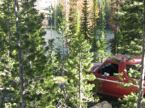 1981 Ford Bronco - A red SUV is partially obscured by trees, parked near a body of water.