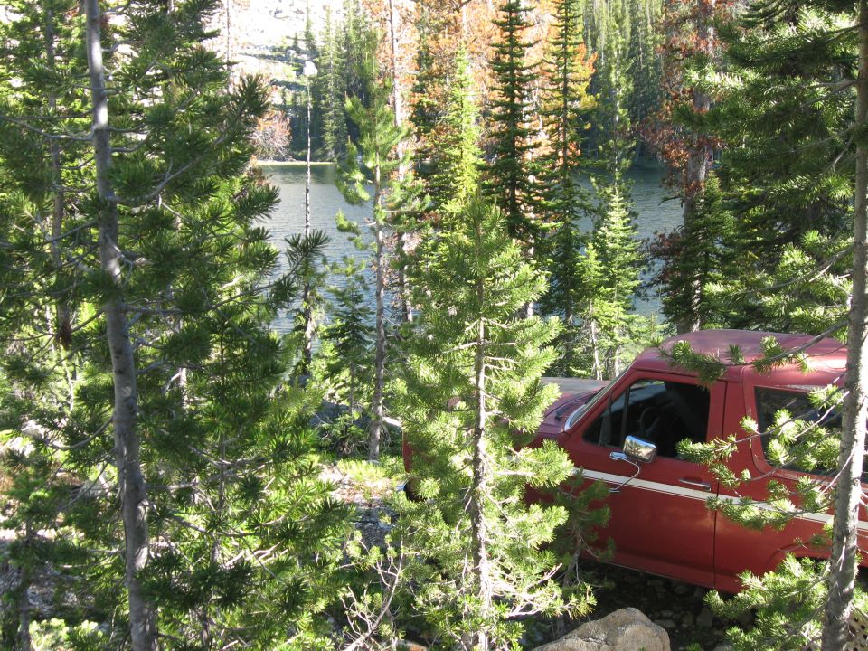 Red SUV parked near a lake, seen from the side and front quarter angle through trees
