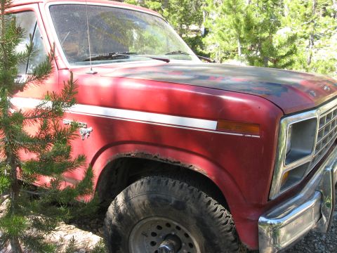 1981 Ford Bronco - A red 1981 Ford Bronco, seen from the front quarter, shows signs of wear and tear with visible rust around the wheel well.