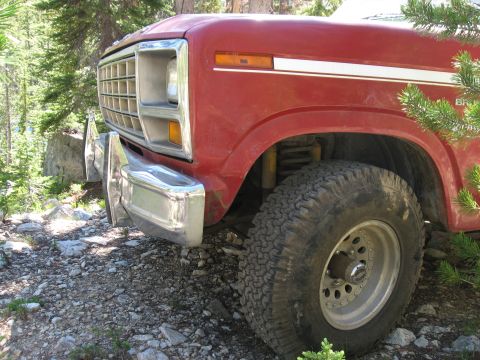 1981 Ford Bronco - A red Ford Bronco is seen from the front quarter panel, parked off-road amongst trees and rocks.