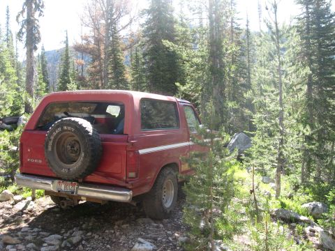 1981 Ford Bronco - A red Ford Bronco is parked on a rocky trail surrounded by trees.