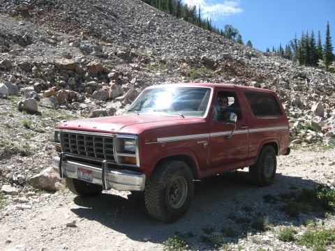 1981 Ford Bronco - A red Ford Bronco is parked on a dirt road in a rocky, mountainous area.