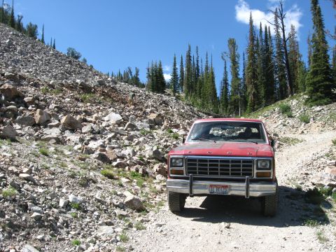 1981 Ford Bronco - Red Ford truck parked on a dirt road in a rocky, forested mountain landscape.