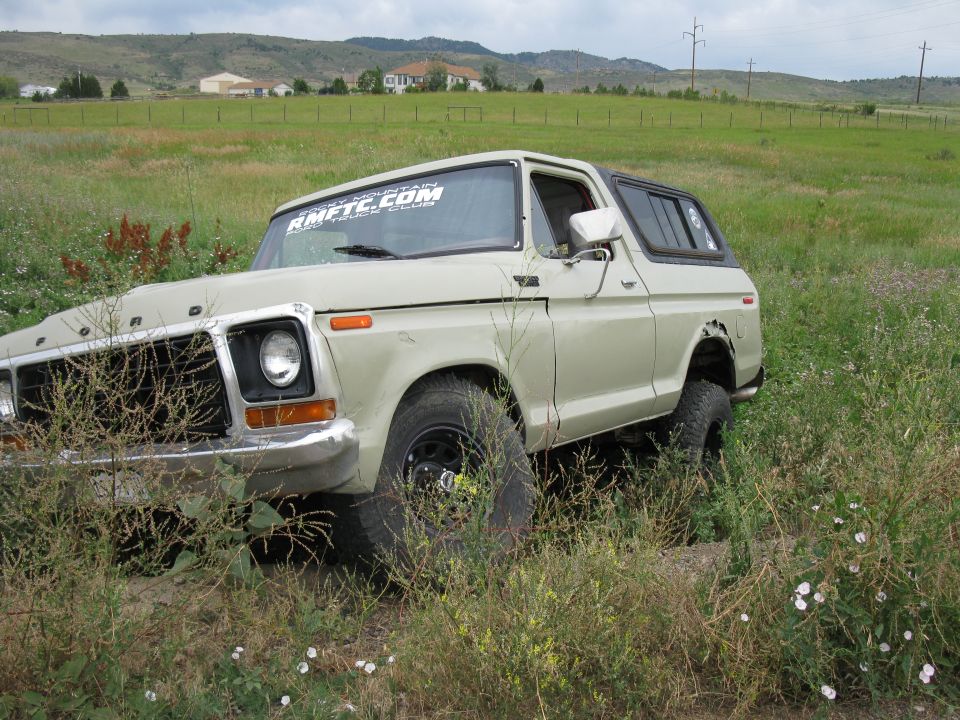 Tan 1978 Ford Bronco with AMFTC.COM sticker on windshield, parked in tall grass