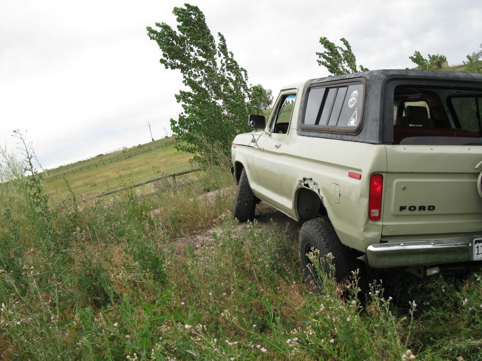Tan 1978 Ford Bronco with black hardtop, rear 3/4 view, dented rear fender, off-road tires