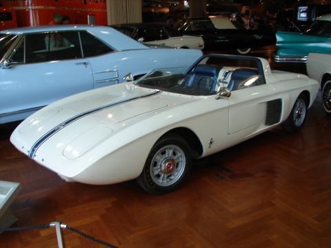 1992 Ford Taurus - A white sports car with blue racing stripes is parked indoors next to other vehicles.