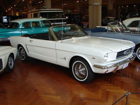 1992 Ford Taurus - A white 1965 Ford Mustang convertible is displayed indoors alongside other vintage vehicles.