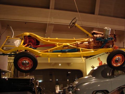 1992 Ford Taurus - A vintage vehicle chassis, complete with engine and steering, is displayed suspended in a museum setting above other classic cars.