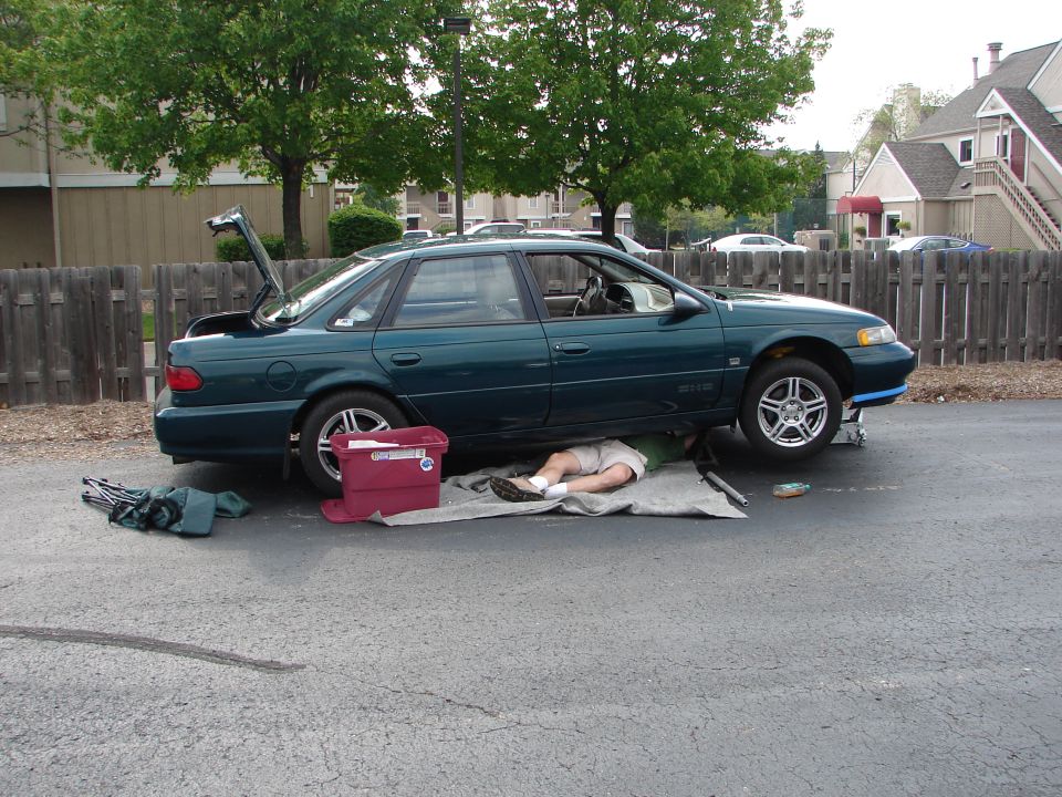 Green 1992 Ford Taurus side view with trunk open and person working underneath
