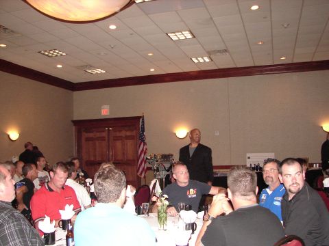 1992 Ford Taurus - A group of people are seated at tables in a banquet hall, with a speaker standing near an American flag.