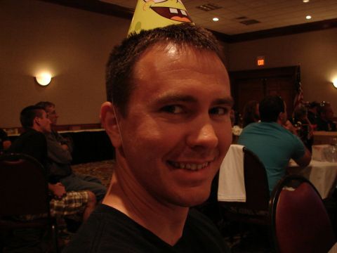 1992 Ford Taurus - A man wearing a Spongebob-themed party hat is smiling at the camera in a room with other people seated at tables.
