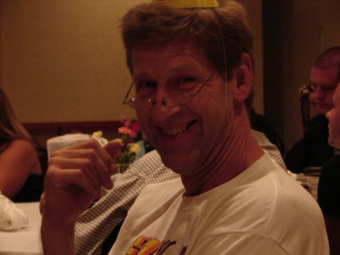 1992 Ford Taurus - A man with glasses and a yellow party hat smiles while sitting at a table with others.