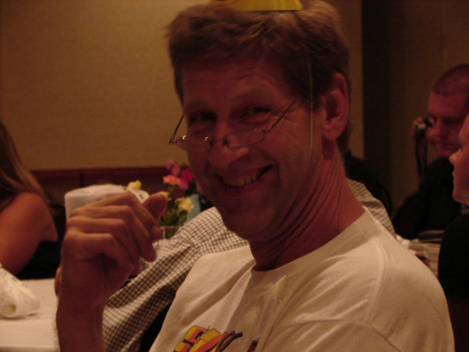 Man wearing glasses and a party hat smiles at the camera