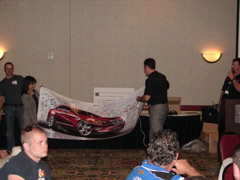 1992 Ford Taurus - A banner displaying a red car is held up at an event.