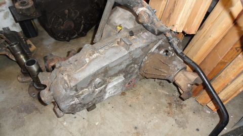 1989 Ford Bronco - A dirty transmission sits on a concrete floor with wooden planks in the background.