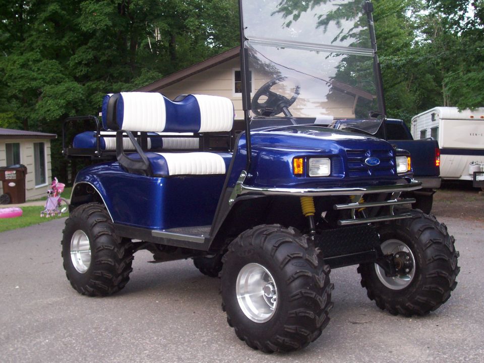 Blue golf cart with white and blue seats, large off-road tires, and a Ford logo on the grille