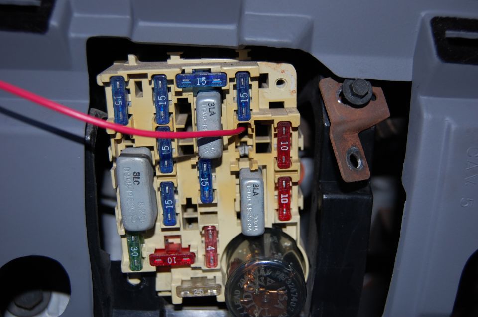 Close-up of a vehicle's fuse box with red and blue fuses, and a red wire connected
