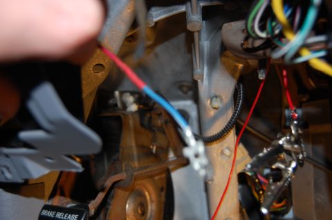 1994 Ford Bronco - Wiring work under a dash, with a hand pulling a red-and-blue wire pair spliced with white butt connectors near the parking brake pedal asse…