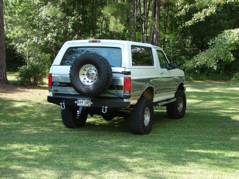 1995 Ford Bronco - This lifted Ford Bronco is parked on a grassy lawn with trees in the background.