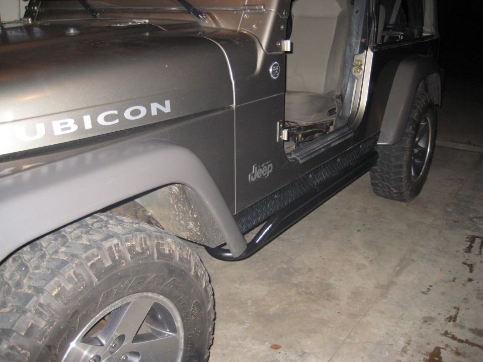 Side view of a gray Jeep Wrangler Rubicon with diamond plate rock sliders and off-road tires