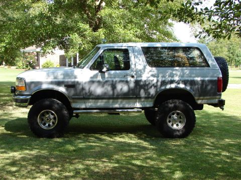 1995 Ford Bronco - A lifted Ford Bronco is parked on a grassy lawn under trees.
