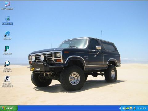 1985 Ford Bronco - A modified Ford Bronco sits on a sandy terrain under a clear blue sky.