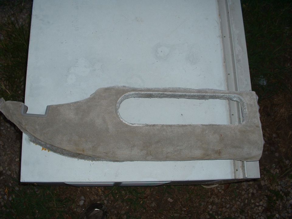 Back side of a gray door trim panel showing fiberboard backing and armrest cutout