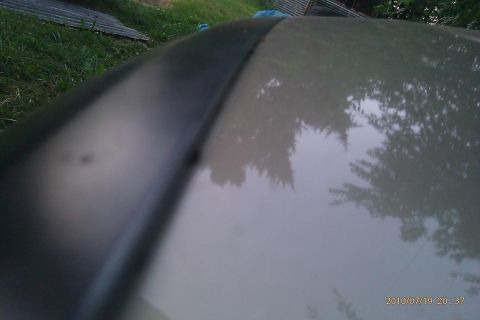 2000 Mercury Grand Marquis - A close-up view of a car's hood shows a dark trim piece and reflections of trees.