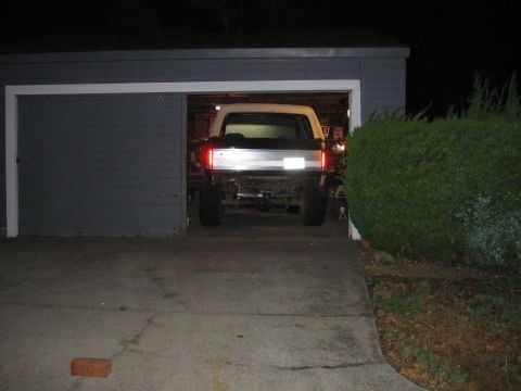 1989 Ford Bronco - A lifted Ford Bronco is partially visible in a dark garage, showing its rear end and large tires.