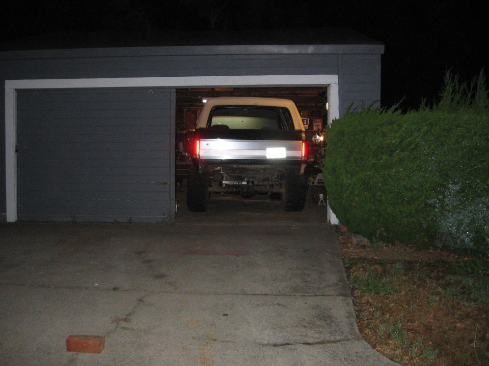 Rear view of a lifted, white Ford Bronco with a silver tailgate strip, parked in a garage