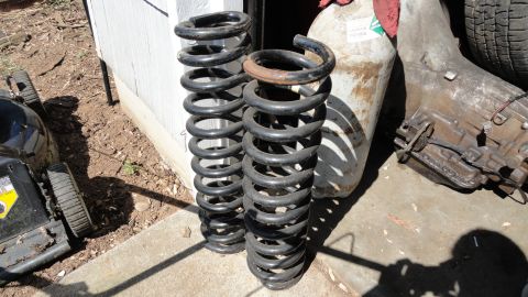 1989 Ford Bronco - Suspension springs and a transmission sit on the ground outside a building, with a lawnmower visible to the left.