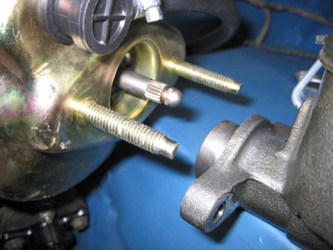 1990 Ford Bronco - Close-up of a gold zinc-plated brake vacuum booster with its two threaded mounting studs and the protruding output pushrod, sitting on a bl…