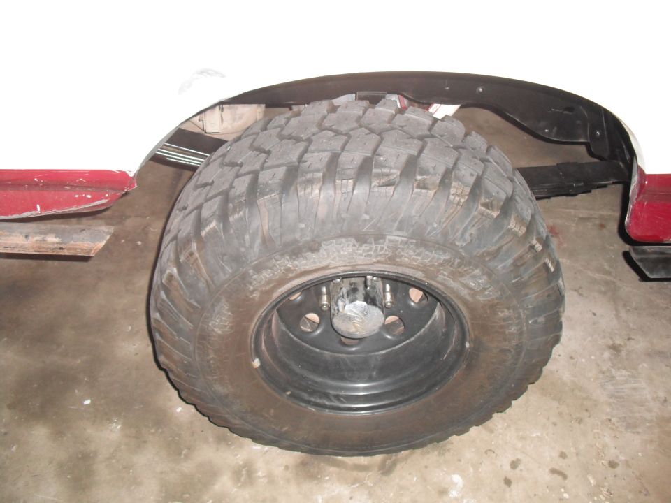 White vehicle's rear wheel and tire with aggressive tread, red fender trim, and leaf springs visible