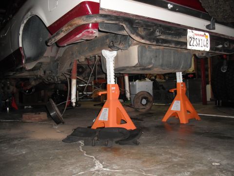 1991 Ford Bronco - The undercarriage of a 1991 Ford Bronco is visible, supported by orange jack stands, with the fuel tank and suspension components exposed.