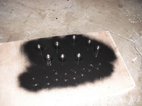 1991 Ford Bronco - Several nuts and washers are laid out on a piece of wood and being spray painted black.
