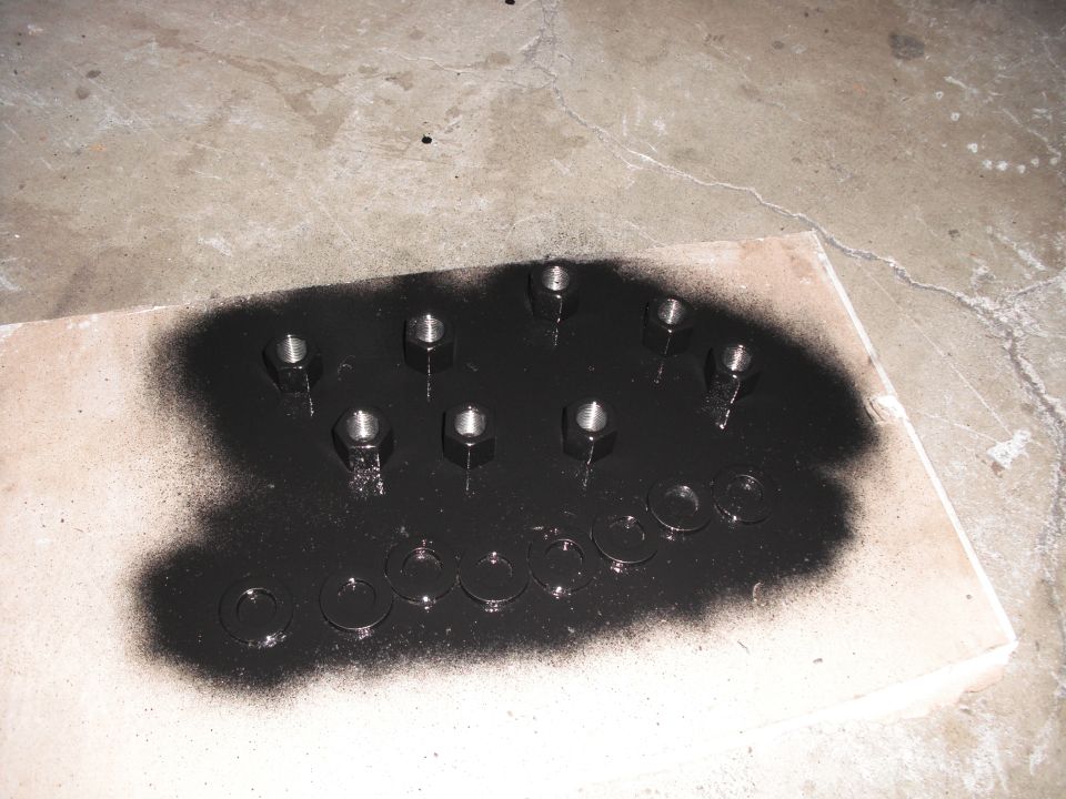 Nuts and washers on a piece of wood, partially covered in black spray paint