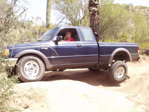 1993 Ford Bronco - Ford Ranger pickup truck navigates a dusty off-road trail with desert vegetation.