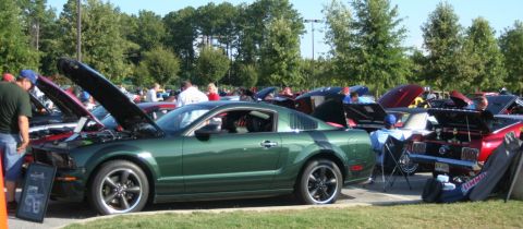 1980 Ford Mustang - A green Ford Mustang coupe is displayed with its hood open at a car show, surrounded by other cars.