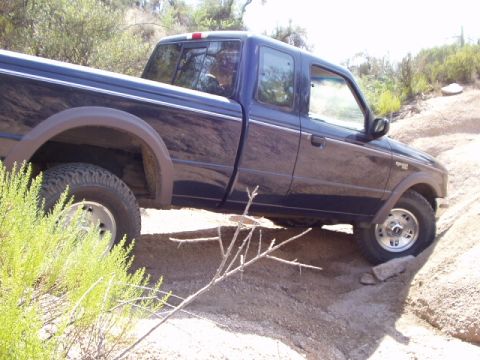 1993 Ford Bronco - A blue Ford Ranger pickup truck navigates a rough dirt terrain.