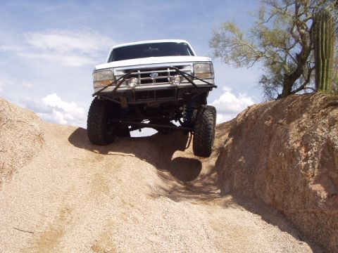 1993 Ford Bronco - A white 1993 Ford Bronco navigates a challenging off-road terrain with large tires and a modified bumper.