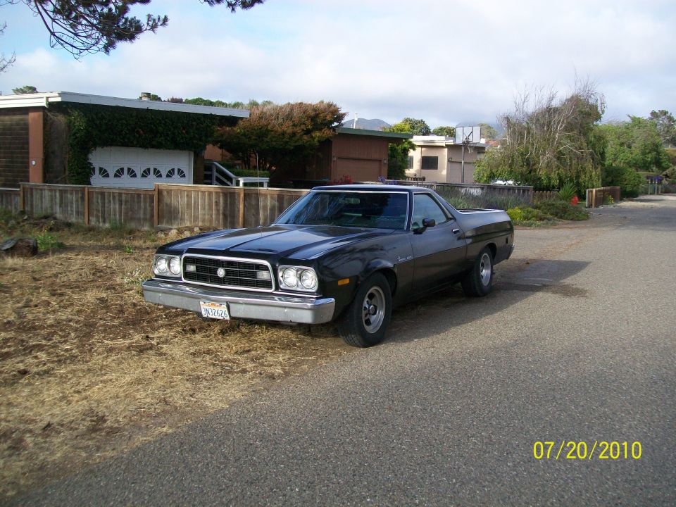 Black 1972 Ford Ranchero parked on a street, front 3/4 view, with a house and fence in the background