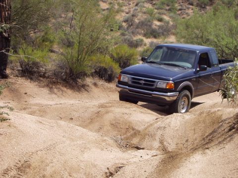 1993 Ford Bronco - A dark blue Ford Ranger navigates a bumpy dirt path in a dry, brushy landscape.